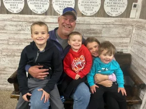 Man sitting on a bench surrounded by four smiling children, showcasing a friendly and family-oriented atmosphere, relevant to NHH Roofing Plus's commitment to community and customer satisfaction.
